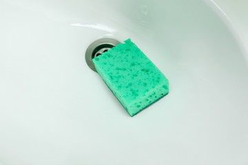 green sponge lie on ceramic washbasin. Housework, cleaning bathroom.