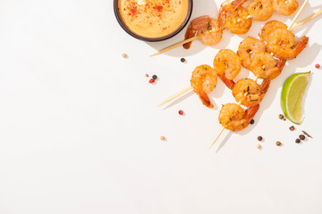 top view of delicious fried prawns on skewers with sauce, lime and pepper on white background