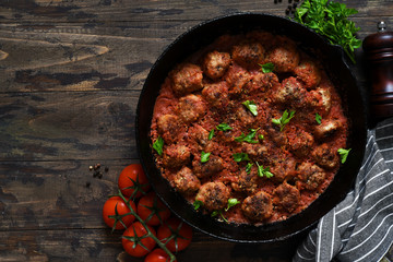 Frying pan with meat balls with tomato sauce on a wooden background.