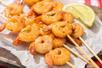 close up view of prawns on skewers with lime on parchment paper on wooden board