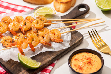 prawns on skewers with lime and sauce on parchment paper on wooden board and plaid napkin on white background