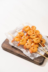 prawns on skewers on parchment paper on wooden board on white background