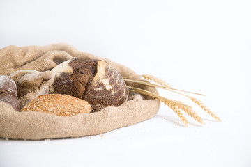 Traditional homemade wheat and rye buns and loafs in rustic jute sack with ears. Side view, closeup, copy space. Isolated object on white background. Bakery or freshly baked bread concept