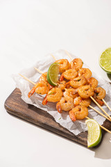 prawns on skewers with lime on parchment paper on wooden board on white background