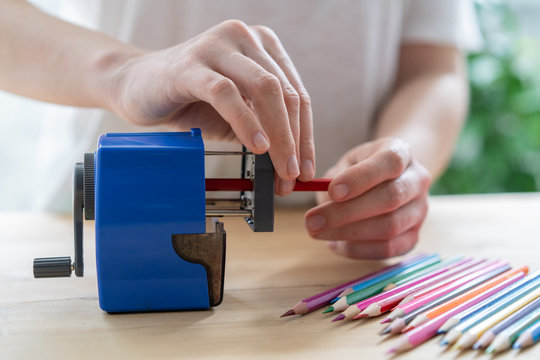 close-up of women's hands using a blue pencil sharpener at the table, school concept