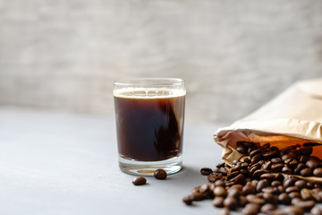 Kaffee in einem Trinkglas und geröstete ganze Kaffeebohnen in einer Papiertüte. Nahaufnahme, rustikaler Stil, grauer Hintergrund.