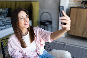Young beautiful woman making selfie photo using cellphone while sitting in chair.