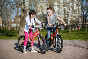 Fototapeta na wymiar Kids riding bikes in a park. Children enjoy bike ride in the city. Brother and sister friends forever. 