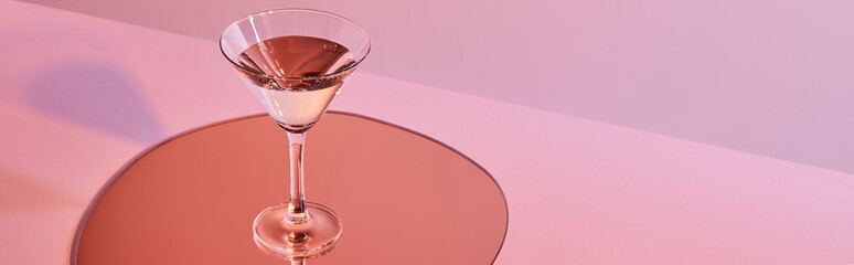 cocktail glass with liquid on mirror with reflection on pink background, panoramic crop