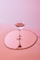 cocktail glass with liquid on mirror with reflection on pink background