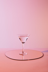 cocktail glass with liquid on mirror with reflection on pink background