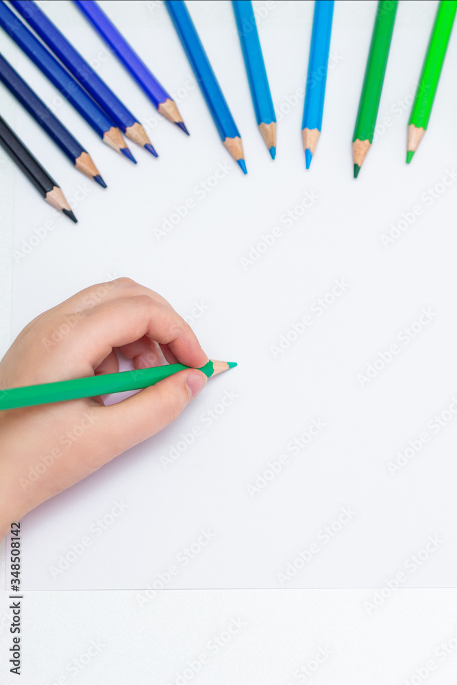 Wall mural Top view of girl's hand drawing on white blank paper by green pencil. Mockup. Empty space for text.