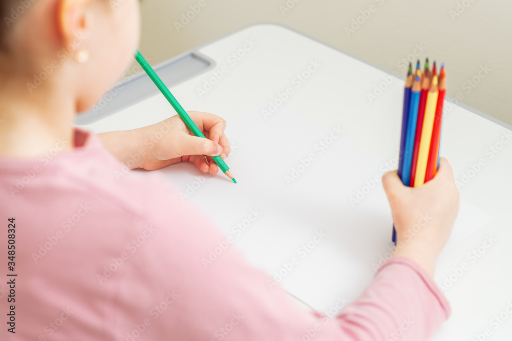 Wall mural little girl's hand drawing by green pencil on blank paper with bunch of colorful pencils in her hand