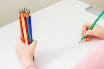 Naklejka premium Child's hand drawing by color pencil on blank paper holding bunch of colored pencils in her hand. Selective focus.