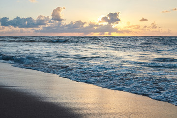 Sunset at the rocky sea. Turquoise water in the ocean in the evening.Yellow sky with small clouds and blue waves at sandy beach at the seaside.Paradise resort landscape.Close-up picture of ocean waves