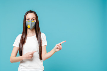 woman pointing fingers at copyspace wearing respirator mask isolated on blue background