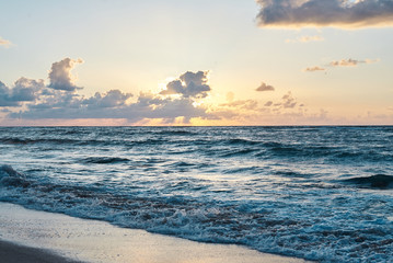 Obraz premium Sunset at the rocky sea. Turquoise water in the ocean in the evening.Yellow sky with small clouds and blue waves at sandy beach at the seaside.Paradise resort landscape.Close-up picture of ocean waves
