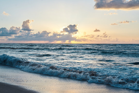 Sunset at the rocky sea. Turquoise water in the ocean in the evening.Yellow sky with small clouds and blue waves at sandy beach at the seaside.Paradise resort landscape.Close-up picture of ocean waves