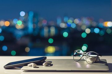 Laptop, smartphone and earphone are turning off put on table with colorful city bokeh lights for...