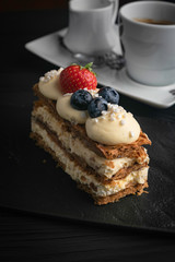 French dessert Milfey cake, with berries on a black plate and a dark background