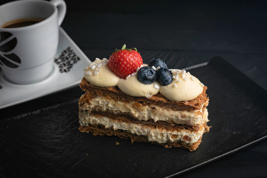 French dessert Milfey cake, with berries on a black plate and a dark background
