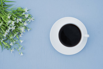 Cup of coffee and wildflowers on a blue table. In the open space. Top view. Breakfast concept

