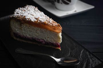 Cheesecake in a black plate with a spoon on a dark background