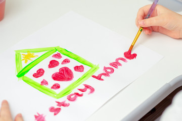 Child's hand drawing Stay Home words and house with hearts by brush with watercolors on white paper at home. Stay Home concept.