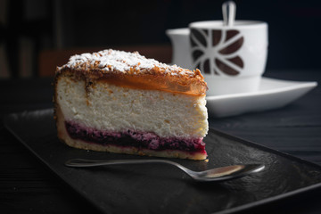 Cheesecake in a black plate with a spoon on a dark background