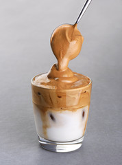 Glass with dalgona coffee and spoon with foam on a gray background. Ice milk and foamy whipped coffee.