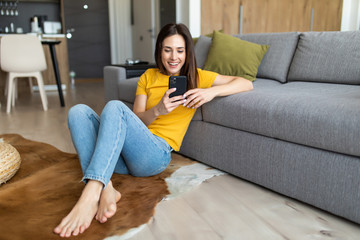 Young woman texting on smartphone. Pretty woman in casual looking at away while sitting on the floor carpet with tablet. Technology and communication concept