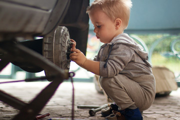 The child repairs the car. The boy changes the wheel. A car on a jack without a wheel.