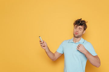 Man with remote controller in outstretched hand suffering from heat on yellow