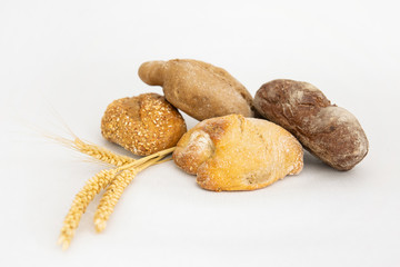 Homemade different breads and ears of wheat. Crunchy loafs made of wheat and rye flour isolated on white background. Studio shot. Side view. Cooking and baking at home concept