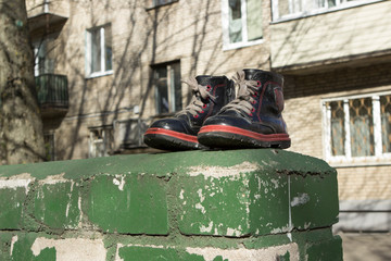 A pair of well-preserved children's boyish black boots is located near a dumpster on the street....