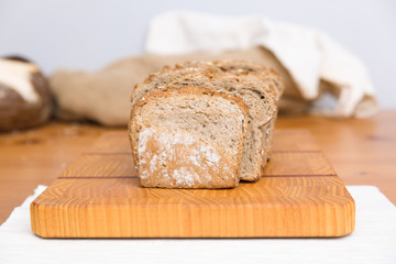 Toasted loaf of wholegrain bread on chopping board. Heap of loafs and buns in background. Bakery or healthy breakfast concept