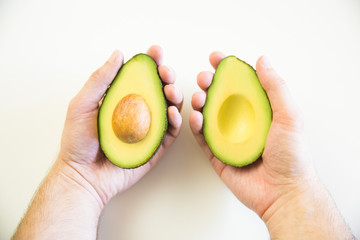 Two halves of avocado with core in human hands. Closeup shot. Isolated objects on white background....