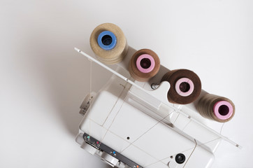 Top view of overlock machine and spools of thread on the white table.Empty space