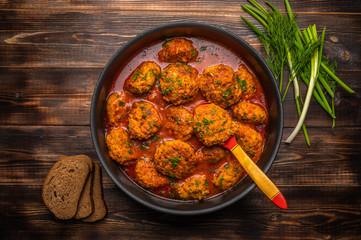 Homemade meatballs in tomato sauce in a saucepan with a wooden spoon. Nearby bread, green onions and dill. Top view