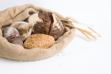 Freshly baked crusty wheat and rye buns and loafs in rustic jute sack with ears. Closeup shot. Isolated object on white background. Bakery or homemade bread concept