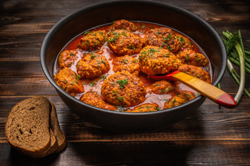 Homemade meatballs in tomato sauce in a saucepan with a wooden spoon. Nearby bread, green onions and dill
