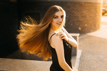 Obraz premium Smiling business woman in black dress sitting. Summer. isolated woman portrait with healthy developing hair. Woman at sunset looks at the camera.
