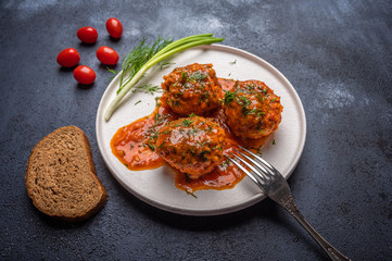 Homemade meatballs in tomato sauce on a white ceramic plate with fork, bread, onions and tomatoes