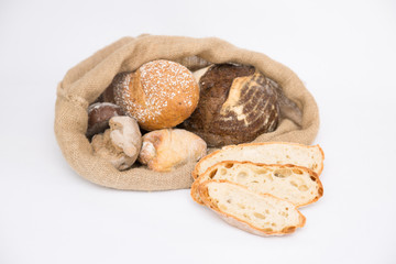 Rustic burlap sack with sliced wheat bread and crusty homemade buns. Isolated object on white background. Baking or traditional bread concept