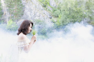 Fototapeta na wymiar Beautiful girl with dark hair in fog with flowers.
