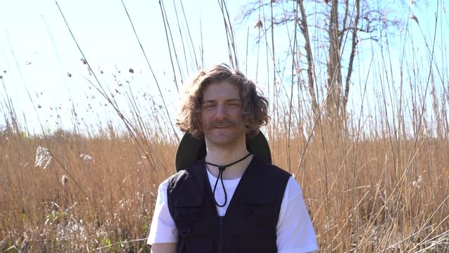 Portrait young handsome caucasian hipster man with moustache nature background wears vest with pockets. Smiling hiker, traveler, hunter or fisherman in outfit by the river on a sunny day