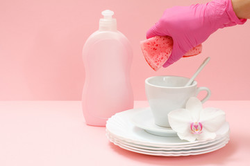Woman's hand in protective glove with a sponge and utensil on a pink background.