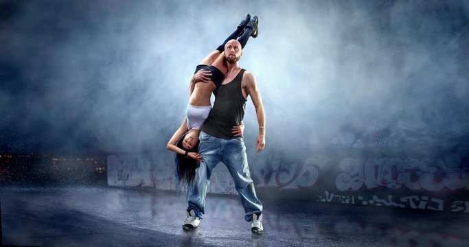 A couple of street dancers in a action with a graffity wall behind the fog on a backgroung.