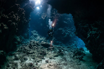 typical underwater cave in a red sea reef with an underwater photographer diver