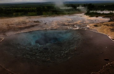 Geothermal valley Haukadalur in South Iceland. Dramatic picture of hot springs and woods in the background.